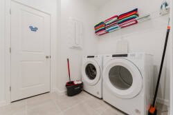Welcome to a bright and functional laundry room, where sleek white appliances harmonize with fresh light walls. Vibrant, neatly folded towels bring a splash of color, and tiled flooring adds practicality to this inviting space.