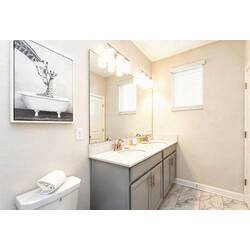 Freshen up in a bright bathroom with a double vanity, large mirror, gray cabinets, warm lighting, marble-style tile, soft towels, and playful wall art.