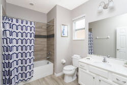 Enjoy a modern bathroom featuring a sleek white vanity and a spacious mirror that enhances natural light. The stylish blue patterned shower curtain adds a vibrant touch to the warm wood accents in the shower area.