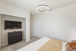 Rest in a bright bedroom with a cozy white bed, soft neutral blanket, modern ceiling light, wall-mounted TV, black dresser, and calm neutral tones, creating a comfortable space for vacation.