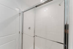 Experience this sleek bathroom with modern glass shower doors and shiny chrome fixtures that create a fresh atmosphere. Bright white tiles reflect light, enhancing the spaciousness and inviting you to relax and unwind.