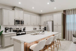 This bright kitchen boasts sleek, light-colored cabinetry and a spacious island with elegant bar stools, ideal for casual dining and socializing. Large windows fill the space with natural light, enhancing the cheerful ambiance.