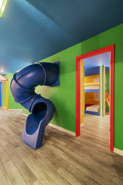 This vibrant playroom, with its fun blue slide and bold green walls, creates an energizing space for kids to explore. The playful colors and sleek flooring invite laughter and adventure, making it perfect for family bonding.