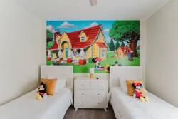 This charming children's room features twin beds with plush character toys, inviting young guests to relax. A vibrant mural of a whimsical cottage adds magic, creating a delightful atmosphere for fun and unwinding.