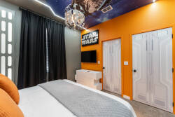 Welcome to this vibrant bedroom, where lively orange walls and a celestial ceiling set a playful mood. Enjoy the cozy bed, stylish white furniture, and dramatic lighting, creating an exciting and relaxing atmosphere for your stay.