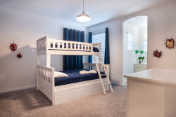This charming bedroom features a cozy white bunk bed, perfect for kids or extra guests, complemented by rich navy curtains that frame the windows. Soft carpeting adds warmth, while playful decor hints at a fun atmosphere.
