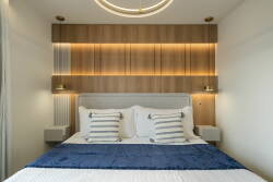 Unwind in this beautifully designed bedroom, featuring a cozy bed with plush pillows, a rich blue throw, warm wooden accents, and soft lighting, all creating a tranquil atmosphere for your ultimate relaxation.