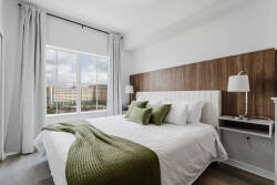 This bright and stylish bedroom features a plush white bed with green accents, creating a refreshing atmosphere. A large window lets in natural light and offers a lovely view to enhance your comfort and relaxation.