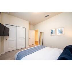Rest in a cozy bedroom with a white bed, blue accent wall, warm bedside lamps, wall-mounted TV, soft curtains, and neutral carpet for vacation comfort.