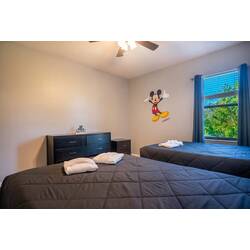This bright and cheerful bedroom boasts two cozy beds with crisp white linens for a restful night. A playful Mickey Mouse mural adds whimsy, and the large window lets in plenty of natural light, creating a welcoming atmosphere.