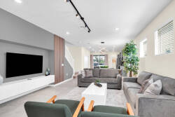 Experience a bright and inviting living area filled with natural light from large windows, featuring soft gray furniture, a cozy sectional sofa, and vibrant green chairs, ideal for relaxation and socializing.