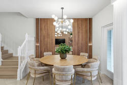 Gather in an elegant dining area with a round wooden table, soft upholstered chairs, modern chandelier, warm wood panels, mirror details, and white curtains, creating a bright space for family meals during vacation.
