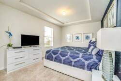 This bright, airy bedroom features a plush white bed with a navy-patterned duvet and soft carpet underfoot. A sleek dresser and modern decor, combined with natural light, create a cozy and inviting atmosphere for your stay.