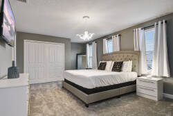 Enjoy peaceful nights in this elegantly designed bedroom, complete with a cozy upholstered bed, fresh white linens, and stylish black accents. Large windows let in natural light, and a chic chandelier adds a sophisticated touch.