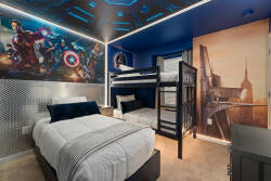 Welcome to a vibrant kids' bedroom with playful superhero murals that spark imagination. The cozy white bedding pairs perfectly with the bold blue walls and metallic accents, creating a fun and comfy retreat for your little ones.