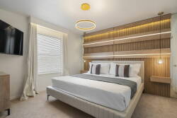 Enjoy restful nights in our beautifully designed bedroom with a plush king-sized bed, soft linens, and warm wood paneling. Cozy lighting sets a relaxing mood, and a sleek TV provides entertainment right at your fingertips.
