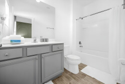 Bright and airy, this bathroom features a sleek gray vanity complemented by warm wood-like flooring, creating a fresh atmosphere. The clean, white tub and shower invite relaxation, ensuring comfort during your stay.