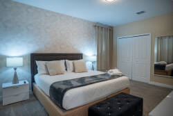 Experience elegance in this beautifully designed bedroom with a plush king-size bed, crisp linens, a chic tufted ottoman, and stylish lamps, all complemented by patterned wallpaper and a large mirror for a warm ambiance.