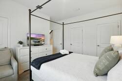 Unwind in this beautifully styled bedroom with a charming four-poster bed and crisp linens. The soft whites and cool blues create a serene atmosphere, enhanced by a cozy armchair, sleek dresser, and a wall-mounted TV for your.