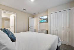 Experience comfort in this cozy bedroom with a plush white bed adorned with a vibrant blue pillow, soft carpeting, and warm, neutral walls. Enjoy entertainment on the sleek wall-mounted TV for your relaxation.