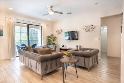 This bright and airy living area boasts soft gray sofas with textured pillows, warm wooden flooring, and large windows that fill the space with natural light. A stylish coffee table invites you to relax and connect with others.