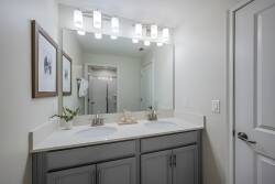Enjoy a stylish bathroom with a sleek dual vanity, light-colored countertop, and modern fixtures. The soft gray cabinetry and bright lighting create a fresh atmosphere, complemented by charming decor accents for a perfect stay.