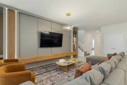 Enjoy a cozy living area with a plush gray sectional and warm orange accent chairs. A stylish wood media console holds a sleek flat-screen TV, and soft lighting enhances the inviting atmosphere for your relaxation.