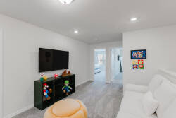 Relax in this bright living area with a cozy white sofa and lively decor, including vibrant artwork and charming figurines. The soft gray carpet adds warmth, while a sleek TV stand enhances this stylish space for your comfort.