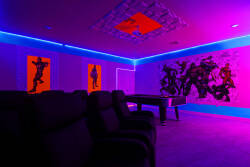 Step into a vibrant entertainment room where bold artwork energizes the space, illuminated by dynamic neon lights. Comfortable seating invites you to unwind, making it an ideal spot for movie nights or game gatherings.