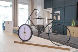 Step into a unique living area where stylish decor meets playful design, featuring a striking bicycle clock that adds a whimsical touch. The soft natural light streams through large windows, enhancing the inviting atmosphere.