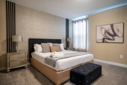 Enjoy tranquil nights in this stylish bedroom with a plush king-sized bed, soft linens, and a chic tufted ottoman. Tall windows fill the space with natural light, enhancing the elegant decor and inviting ambiance.