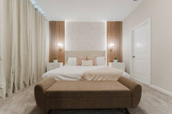 Experience tranquility in a serene bedroom with a plush king-sized bed dressed in soft white linens and stylish pillows. Warm wooden accents and elegant sconces enhance the cozy ambiance, while charming floor-to-ceiling curtains.