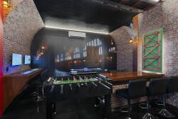 Experience our lively game room with exposed brick and dark wood accents. Join friendly foosball matches or relax at the sleek bar with high stools, all under stylish lighting that creates an energetic ambiance for everyone.