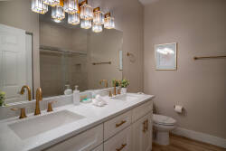 The bathroom boasts a chic double vanity with a white countertop and elegant gold fixtures, enhancing sophistication. The soft glow from the crystal chandelier provides a warm ambiance, ideal for unwinding after your day's.