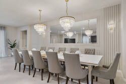 Gather in an elegant dining room with a long table, plush chairs, crystal chandeliers, mirrored wall, and soft neutral decor, perfect for family meals during vacation.