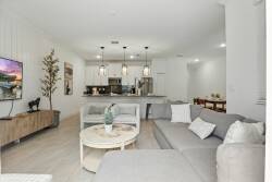 Welcome to a stylish living area with a cozy gray sectional and light wood flooring. The open layout leads to a modern kitchen with sleek pendant lighting, creating a relaxing, bright space for you to enjoy.