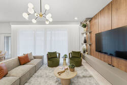 Relax in a stylish living room with a cozy sectional, green accent chairs, wall-mounted TV, warm wood feature wall, soft white curtains, modern lighting, and elegant decor for vacation moments.