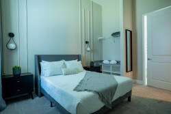 This cozy bedroom features a plush bed adorned with soft linens, perfectly complemented by stylish nightstands and modern wall sconces that enhance the natural light. The elegant decor invites relaxation, making it an ideal stay.