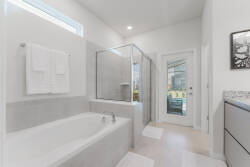 This bathroom boasts a sleek freestanding tub and a spacious glass shower, illuminated by natural light from large windows. The neutral tones and modern fixtures create a fresh, inviting space ideal for relaxation.
