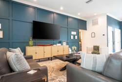 Enjoy a stylish living area with a striking navy accent wall, a plush grey sofa, and a chic coffee table. Warm wood cabinetry and soft lighting create a cozy atmosphere, ideal for your relaxation and comfort.