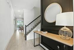Welcome to a stylish entryway featuring a striking black wall that contrasts with soft neutral tones. A sleek console table with a glass lamp complements the natural light streaming through the window, inviting you to explore.