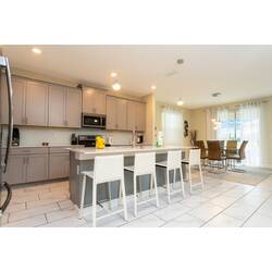 Cook and gather in a bright open kitchen with gray cabinetry, stainless steel appliances, a large island, white bar seating, pendant lights, and a connected dining area with soft curtains.