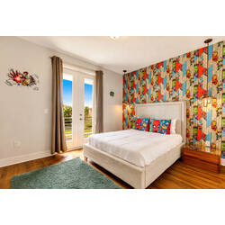 Rest in a bright superhero themed bedroom with a cozy upholstered bed, colorful comic-style accent wall, themed pillows, balcony doors, warm wood flooring, and fun wall details.