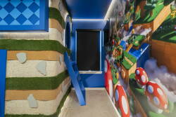 Enter a whimsical world of vibrant blue walls and playful graphics, where textured grass and cheerful mushrooms set the stage for fun and adventure, making it a perfect place for kids and the young at heart to explore and enjoy.