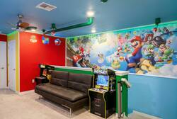 Have fun in a colorful Super Mario game room with arcade machines, cozy sofa, bright wall art, neon signs, ceiling fan, and playful decor, perfect for family entertainment during vacation.