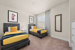 This bright bedroom features two cozy beds with vibrant yellow bedding and plush gray headboards. Playful wall art adds whimsy, and natural light filters through the window, creating a warm and inviting atmosphere for your stay.