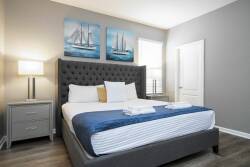 Enjoy the comfort of this stylish bedroom with a plush tufted headboard and crisp white linens that create a soothing ambiance. Sailboat artwork adds color, and natural light filters in, enhancing the inviting atmosphere.