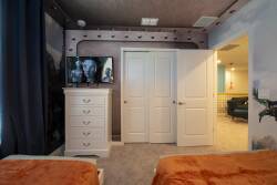 Relax in a cozy bedroom with two inviting beds adorned with warm orange throws, ideal for unwinding after your adventures. Enjoy the plush carpet, stylish furnishings, and a mounted TV for your ultimate comfort and convenience.