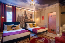 Experience a whimsical bedroom with two stylish beds, playful character pillows, and rich red accents. Warm lighting and a captivating mural create a unique atmosphere, making your stay truly special and adventurous.