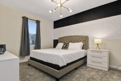 This cozy bedroom features a plush bed with a stylish headboard, complemented by textured white and black accent walls that create a chic atmosphere. Natural light pours in through the window, enhancing the inviting decor.